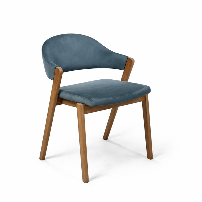 The Camden Dining Chair features a modern, minimalist design with a curved blue velvet-upholstered seat and backrest, plus angled wooden legs. Shown against a white background.