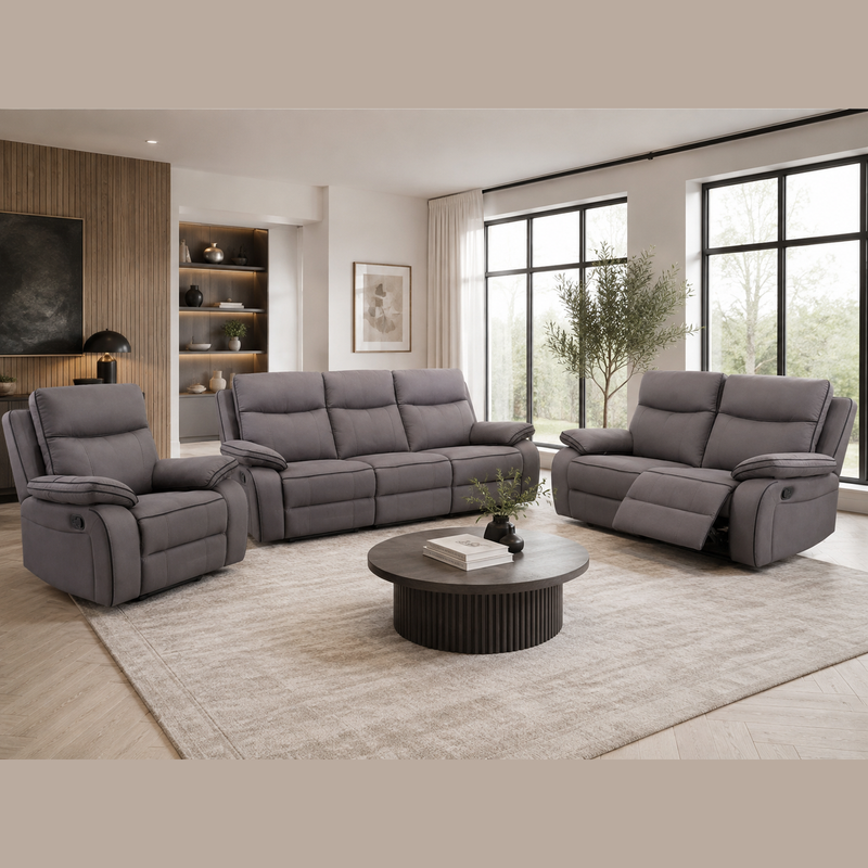 Modern living room featuring the Harper Recliner Range - Special in dark grey fabric, complemented by a round coffee table, light rug, large windows, and built-in shelves adorned with decor. Neutral tones and a minimalistic design enhance the cozy, inviting atmosphere while the contemporary recliner from the Harper range adds both comfort and style.
