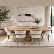 A modern dining room features the Marlo 200cm Table paired with six Willow chairs on a light rug. A potted plant and bowl decorate the table, while abstract art and a tall plant enhance the neutral-toned space.