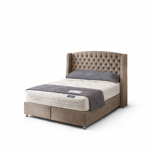 The Ambassador Storage Bedframe features beige velvet upholstery and a tufted headboard, displayed with a cream mattress, gray blanket, and gray pillow against a white background.