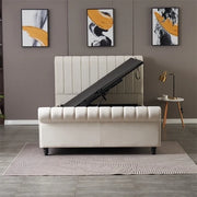 A modern bedroom showcases the Ascot Storage Bedframe in beige, lifted open to reveal hidden storage. The space includes three abstract artworks, a round side table with a lamp, and a patterned rug on tiled flooring.