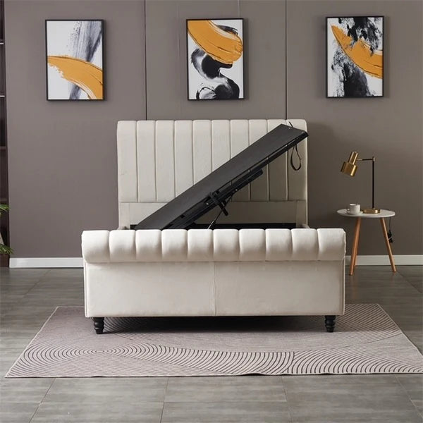 A modern bedroom showcases the Ascot Storage Bedframe in beige, lifted open to reveal hidden storage. The space includes three abstract artworks, a round side table with a lamp, and a patterned rug on tiled flooring.