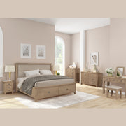 A modern bedroom featuring light wood furniture, including the Aylesbury bedframe, matching nightstands and dressers, a vanity, beige walls, wood floors, a large window, simple decor with framed art, and fresh flowers.