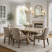 A bright, elegant dining room features the Marlo Dining Table with a grey wash lacquered top, six beige upholstered chairs, a chandelier, and white flowers. Light streams in through large windows with cream curtains.