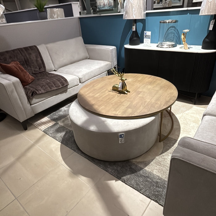 A modern living room showroom featuring two light gray sofas, the Todi Round Coffee Table & Stool Set, table lamps, and framed art on a blue accent wall, all arranged over a beige tiled floor.