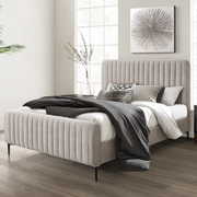 A modern bedroom featuring the Clarissa Bedframe in grey fabric with a vertically lined headboard, white and gray bedding, decorative pillows, a cozy blanket, large window, minimalist artwork, and a vase with branches.