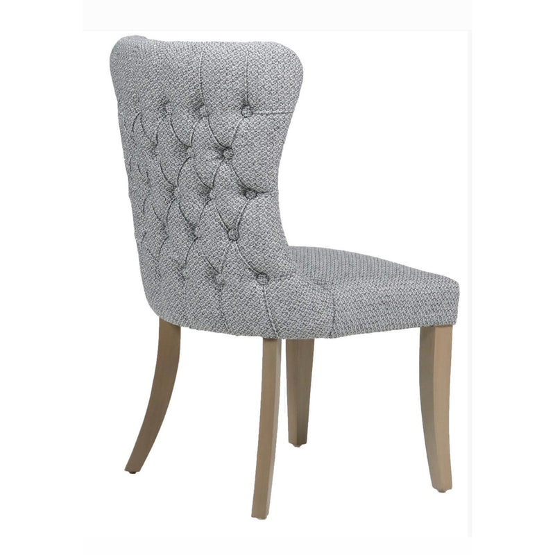 The Duke Chair is a grey upholstered dining chair featuring a button-tufted backrest and light oak legs, displayed at an angle from the back and side.