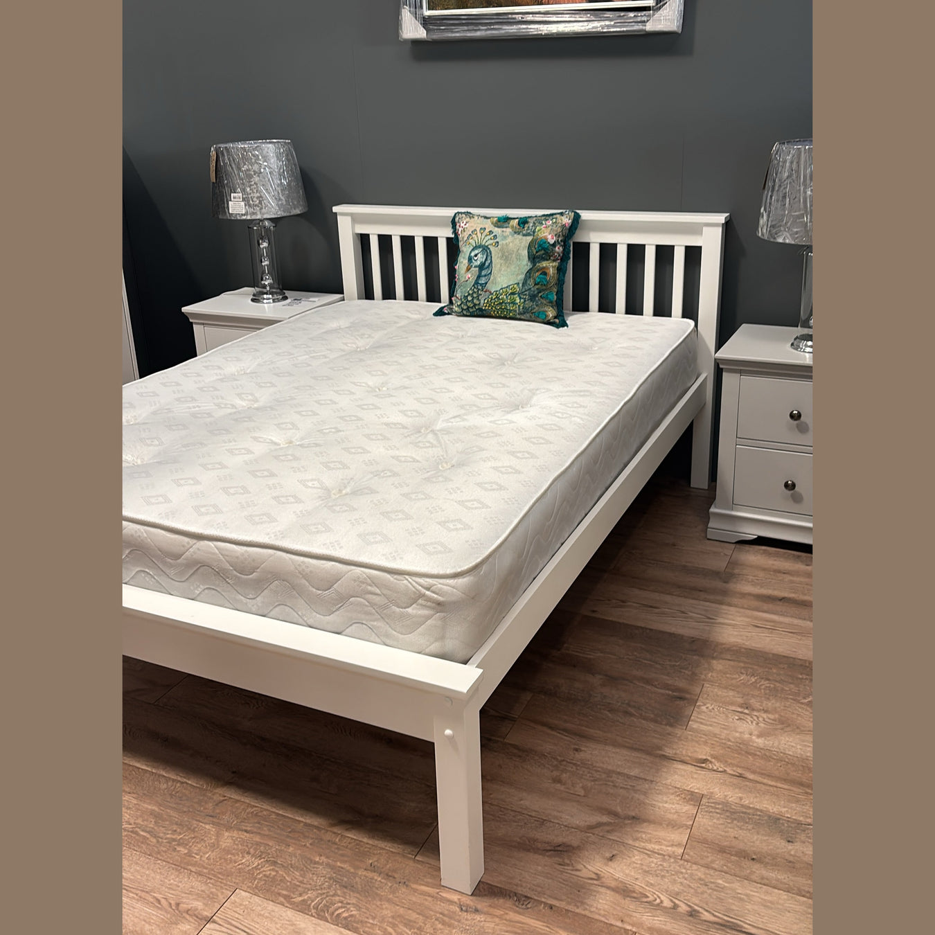 Classic white wooden bed frame with slatted headboard, shown with a mattress and two grey nightstands.