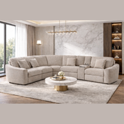 A modern living room featuring the Velora Corner Group sectional in beige chenille, a marble coffee table with gold base, light gray rug, floor lamp, wooden built-in shelves, and large windows that let in natural light.