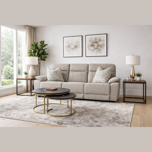 A modern living room featuring the Jude Recliner in light gray, patterned pillows, two round coffee tables, a rug, side tables with lamps, potted plants, and framed abstract art on a white wall near a large window.