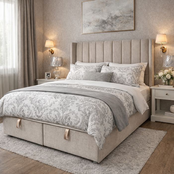 Elegant bedroom featuring the Hilton Storage Bedframe with a beige upholstered winged headboard, patterned bedding, soft gray throw, bedside tables with lamps and flowers, large abstract art above the bed, and natural light through window curtains.