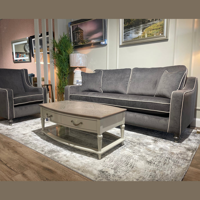 A modern living room with the Irish-made Emperor Range: a gray Aqua Clean sofa and matching armchair, light coffee table with drawer, patterned rug, framed wall photos, all on wooden flooring.