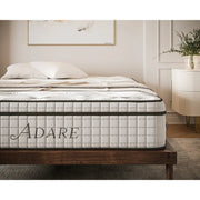 A neatly made bed features the thick, patterned Adare Mattress on a wooden frame in a modern bedroom with neutral decor and a small white nightstand with a plant. The Adare Mattress, with pocket springs, brings comfort and elegance to the space.