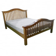 The Saoirse Bedframe is a chunky solid oak bed with matching headboard and footboard, both featuring vertical slats and curved tops. A plain white mattress completes its classic, timeless design.