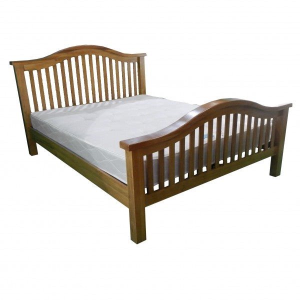 The Saoirse Bedframe is a chunky solid oak bed with matching headboard and footboard, both featuring vertical slats and curved tops. A plain white mattress completes its classic, timeless design.