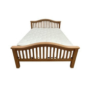 The Saoirse Bedframe is a chunky solid oak bed with a curved slatted headboard and footboard, topped with a white mattress for timeless comfort and style.