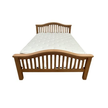 The Saoirse Bedframe is a chunky solid oak bed with a curved slatted headboard and footboard, topped with a white mattress for timeless comfort and style.