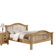 The Saoirse Bedframe, a chunky solid oak bed with a slatted headboard and footboard, features neutral bedding and pillows. Beside it sits a three-drawer wooden nightstand topped with a lamp and stacked books.