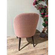 A Slim dining chair with pink herringbone upholstery and dark wooden legs stands on a wooden floor beside a green and pink flowering plant in a gray pot, facing away from the camera.