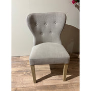 Single light-colored fabric dining chair with a small four-button tufted detail on the back, set on a wood floor.