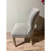 The Jacob chair, with light gray aqua clean fabric and grey washed wood legs, features a high curved backrest. It is shown from the side on a wooden floor against a plain light-colored wall.