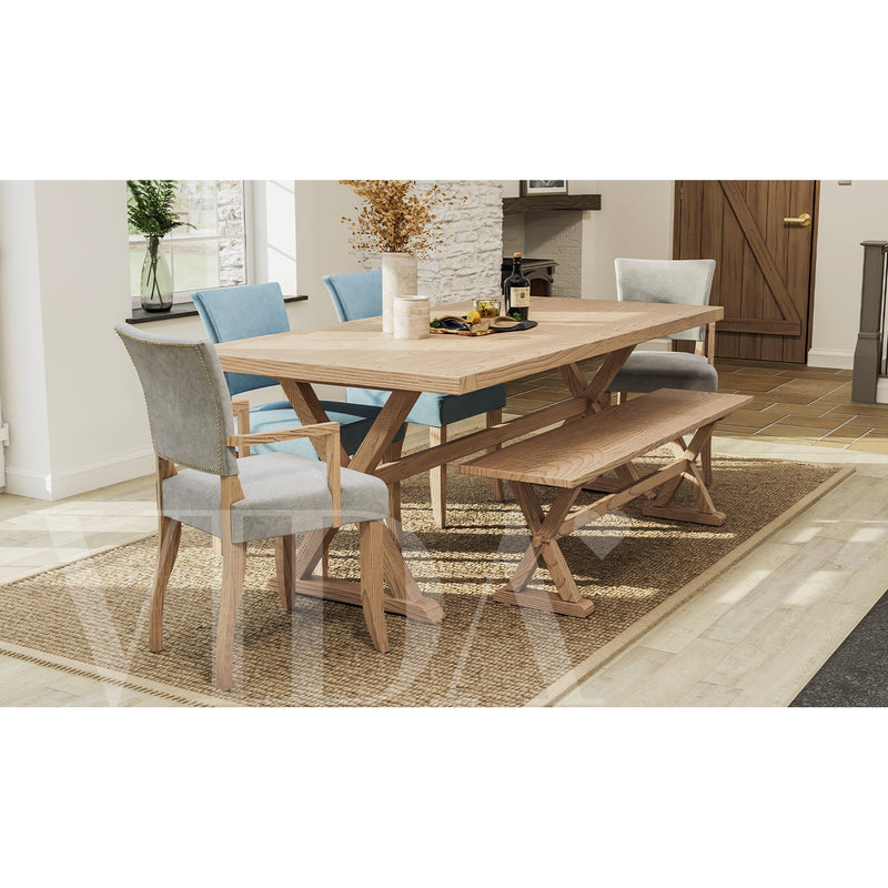 A Duke Dining Chair in mixed blue and gray washable velvet sits with a wooden table, oak legs, matching bench, woven rug, decorative vases, and tableware in a light-filled dining room with large windows.