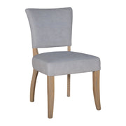 The Duke Dining Chair features a modern, minimalist design with slightly curved oak legs and an upholstered light gray washable velvet seat and backrest.