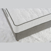 A close-up of the King Koil Paradise Mattress shows its white textured top, gray sides, and Flex-edge border supports, placed on a fluffy white rug.