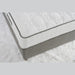A close-up of the King Koil Paradise Mattress shows its white textured top, gray sides, and Flex-edge border supports, placed on a fluffy white rug.