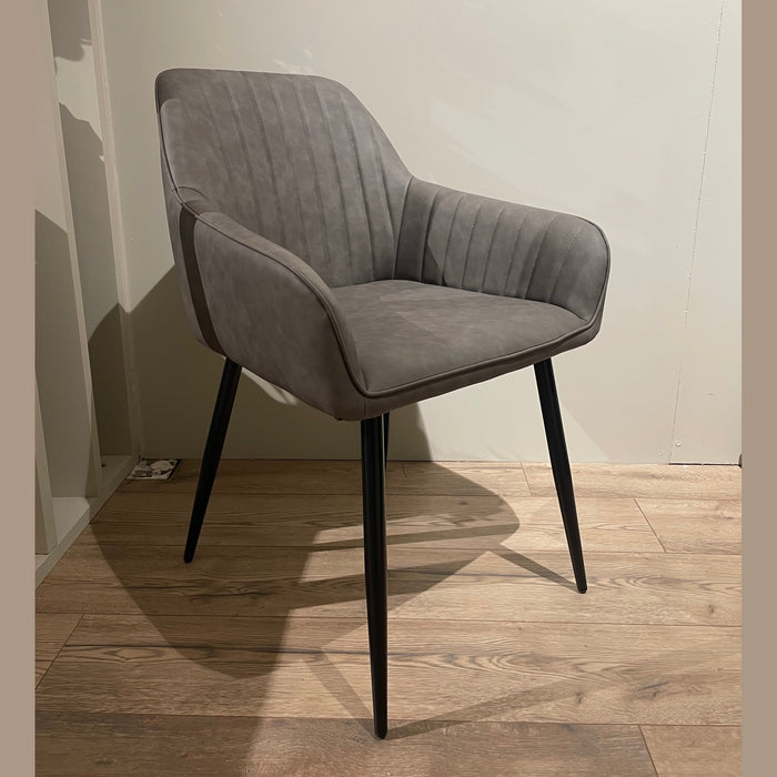 The Enzo Dining Chair offers cushioned gray leatherette seats, black metal legs, and a curved back with vertical stitching, creating a modern touch on light wood flooring backed by an off-white wall.