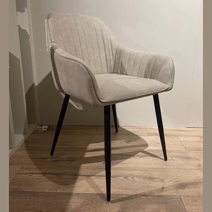 The Enzo Dining Chair has cushioned seats, light gray leatherette upholstery, and slim black legs. Its gently curved back with vertical stitching creates a modern look against a plain light wall and wooden floor.