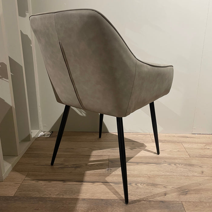 The Enzo Dining Chair, featuring light gray cushioned seats and angled black legs, stands on a wooden floor in a minimalist room with light-colored walls.