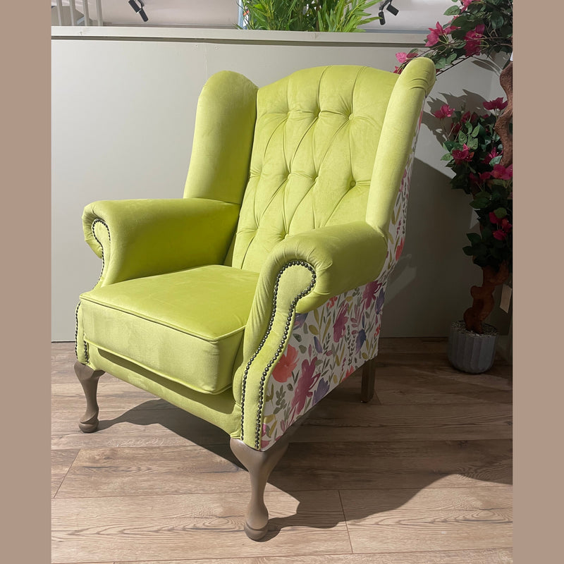 A lime green Queen Anne Chair with tufted back, winged sides, and patchwork outer fabric stands on wooden legs atop a light wood floor, accented by plants in the background—an elegant Irish-made piece.
