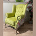 A lime green Queen Anne Chair with tufted back, winged sides, and patchwork outer fabric stands on wooden legs atop a light wood floor, accented by plants in the background—an elegant Irish-made piece.