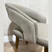 A close-up of the Willow Dining Chair showcases its light gray upholstery, textured outer backrest, and wooden legs—an elegant modern chair that stands out against a neutral wall and light wood floor.