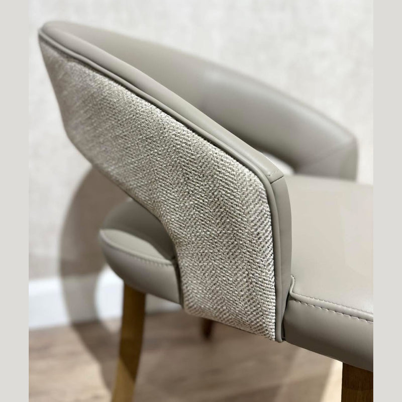 A close-up of the Willow Dining Chair showcases its light gray upholstery, textured outer backrest, and wooden legs—an elegant modern chair that stands out against a neutral wall and light wood floor.