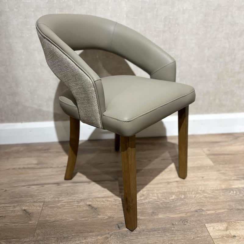 The Willow Dining Chair showcases a curved back, light gray upholstered seat and backrest, and wooden legs, offering modern style ideal for dining spaces with light wood flooring and a textured beige wall backdrop.