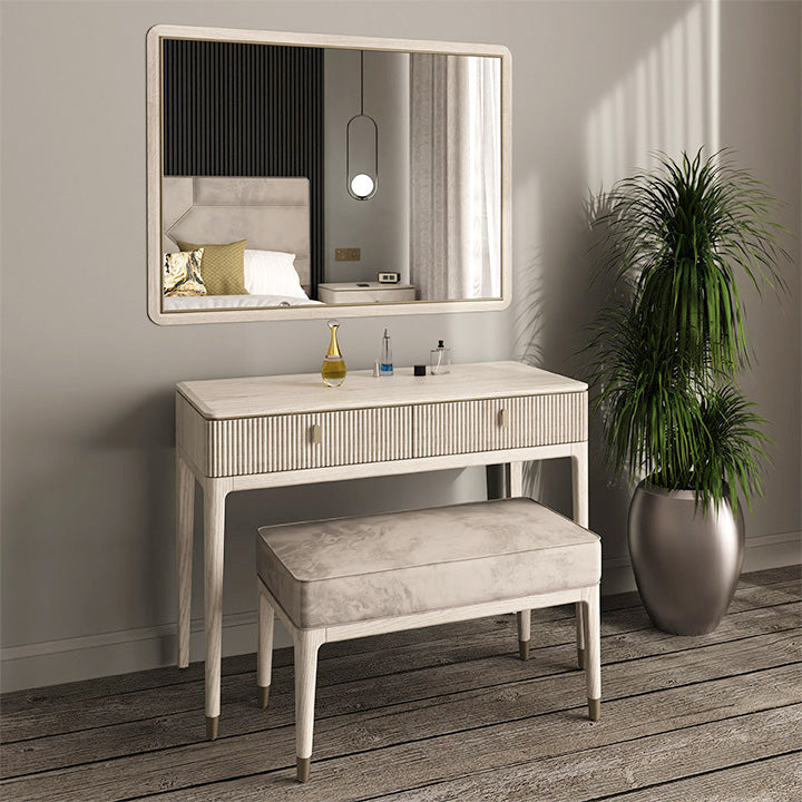 The Diletta Dressing Table has a marble top, ribbed drawers, an upholstered bench, large mirror, and decor accents next to a tall potted plant on a wooden floor in a bright bedroom.
