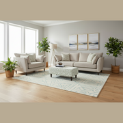 A modern living room features the grand Irish-made Layla beige sofa in washable Aquaclean fabric, a patterned ottoman, large windows, potted plants, a floor lamp, and three abstract paintings on gray walls with light wood flooring and a blue rug.