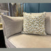 The Layla grand sofa, in beige and made in Ireland with washable aquaclean fabric, showcases a cushion with geometric patterns in muted green, gold, and white. Modern decor is seen in the background.