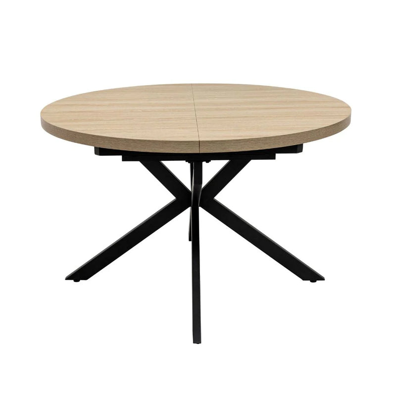 The Dalton 1.2 Round Extending Table features a light wood finish, a central split for extension, and intersecting black metal legs, set against a plain white background.