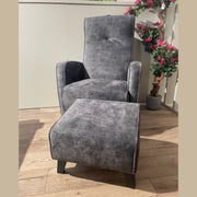 The gray Kelvin Chair and its matching footstool rest on a wooden floor, with pink flowers and greenery in the background as sunlight streams down.