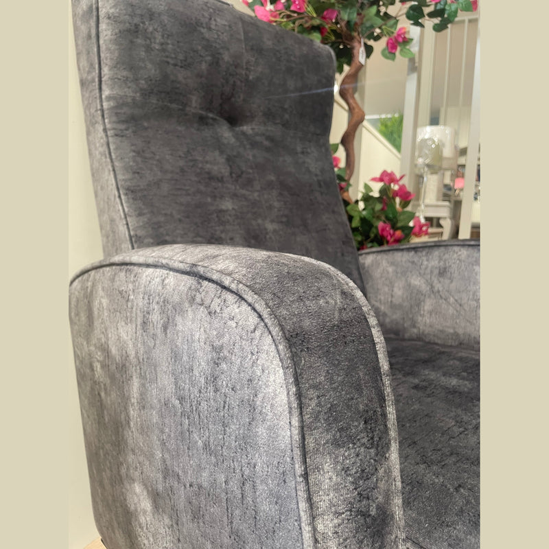 A close-up of the Kelvin Chair showcases its plush, textured gray upholstery and high backrest. Pink flowers, green leaves, and a staircase in the background enhance its elegant presence.