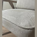 A close-up of the Willow Chair with light gray beige upholstery, wooden armrests, and textured fabric on a cushioned seat, set on a wooden floor against a plain light wall.