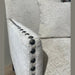 Close-up of the Sylvia Chair with light beige upholstery and black beaded details on the armrest. Includes matching cushion; blurred plant in background.