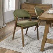 A Camden Dining Chair in olive green velvet adds style to a modern dining room with wooden floors, a wood table, sideboard, and a patterned light gray rug.