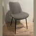 The Lilly Dining Chair features modern gray faux leather and angled black legs, shown on a wooden floor against a plain light-colored wall.