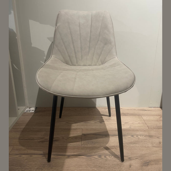 The Lilly Dining Chair features beige upholstery, angled black legs, and a curved backrest with subtle stitching—perfect as a modern accent piece for any space. It sits stylishly on light wood flooring against an off-white wall.
