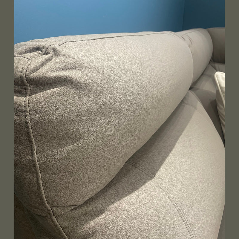 Close-up of the Chloe Corner Group, a modern light gray leather sofa with a cushioned headrest, set against a blue wall. A white pillow and white railing are visible in the background.