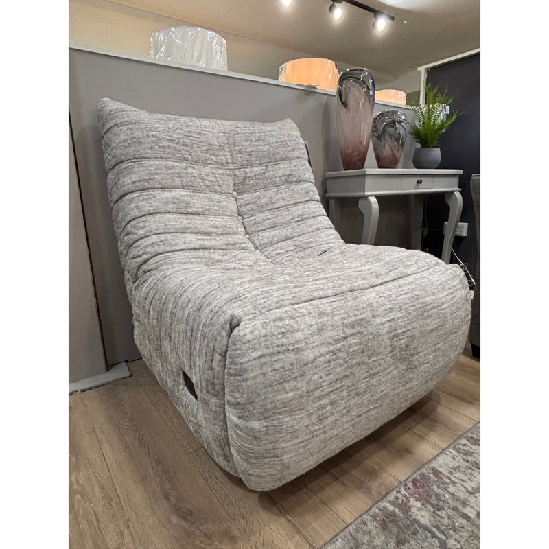 The Ryder Occasional Chair, in light gray with a plush curved design and 360° swivel, rests on a wooden floor beside a gray console table decorated with various items and a green plant.